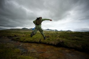 Man hiker jumping across small river
